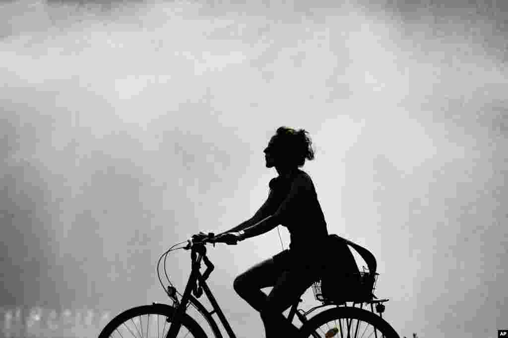A woman on a bike is silhouetted against a water fountain on a bright sunny day in Berlin, Germany.