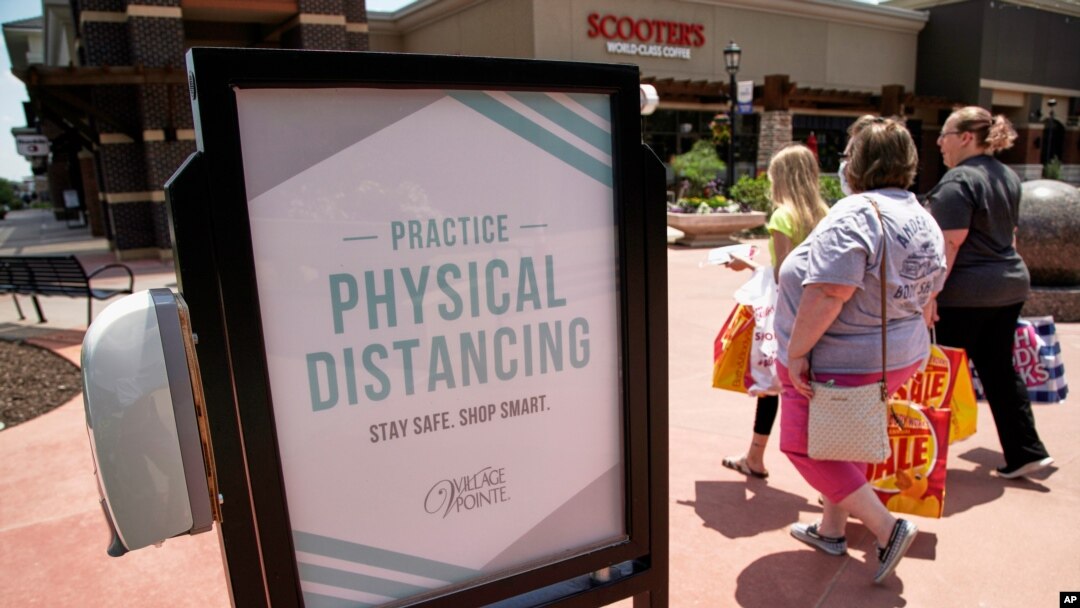 FILE - Shoppers carry their bags past a hand-sanitizing station at the Village Pointe shopping mall in Omaha, Neb., June 16, 2020. 