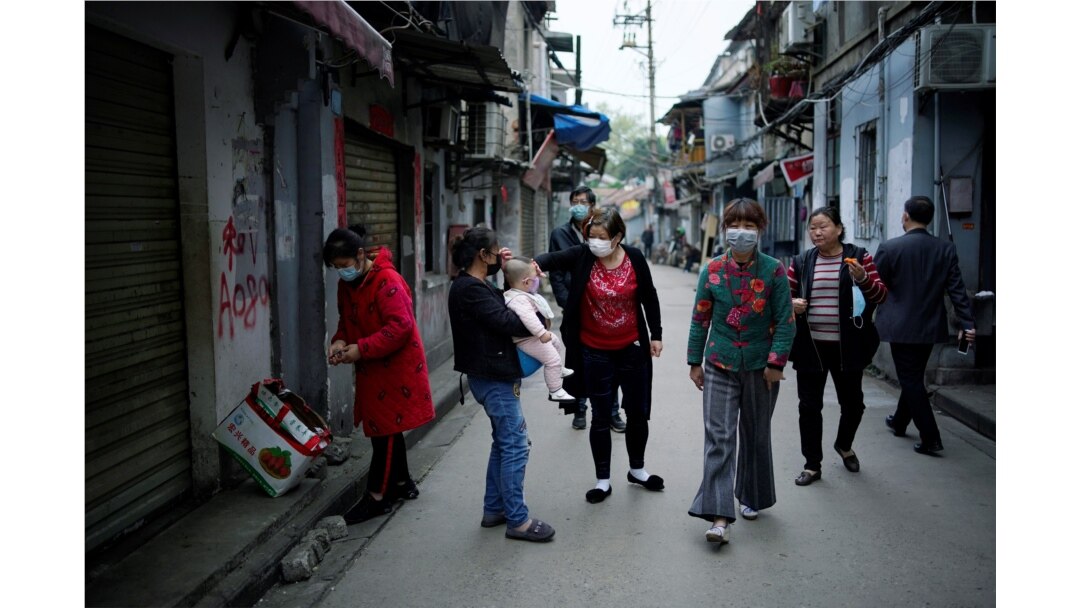 FILE - Residents wearing face masks walk at an old residential community blocked by barriers in Wuhan, Hubei province, the epicentre of China's coronavirus disease (COVID-19) outbreak, Apr. 5, 2020.