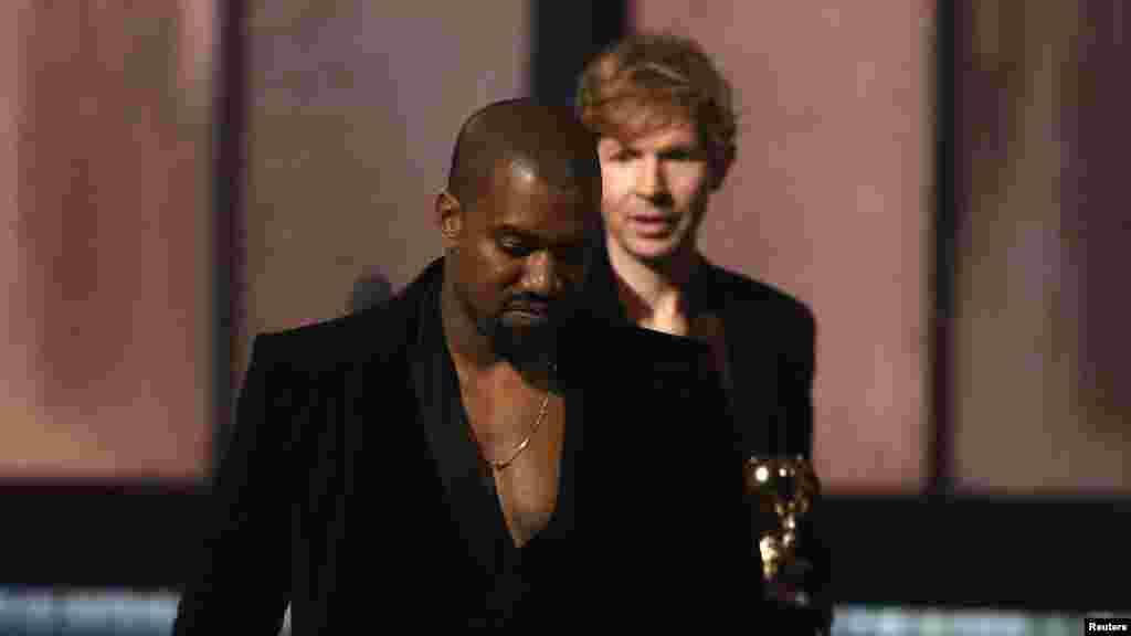 Beck, atrás, observa Kanye West, que subiu ao palco depois de Beck ter recebido o Grammy para Melhor Album do Ano com "Morning Phase". West já o tinha feito na gala do ano anterior, quando tirou o galardão a Taylor Swift na 57ª gala anual dos Prémios Grammy, Los Angeles, Califórnia, Fev. 8, 2015.